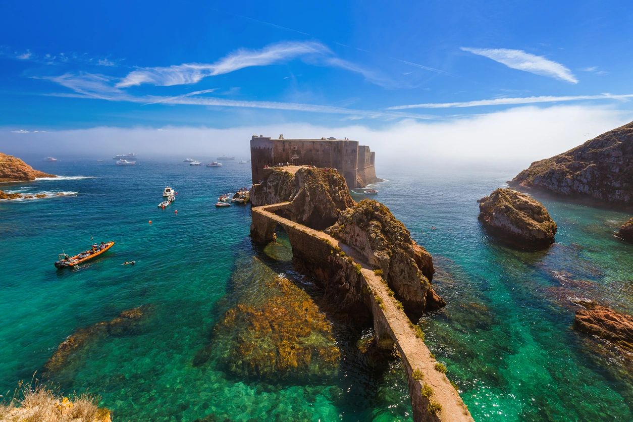 Ancient stone fortress connected by a narrow walkway over turquoise waters.