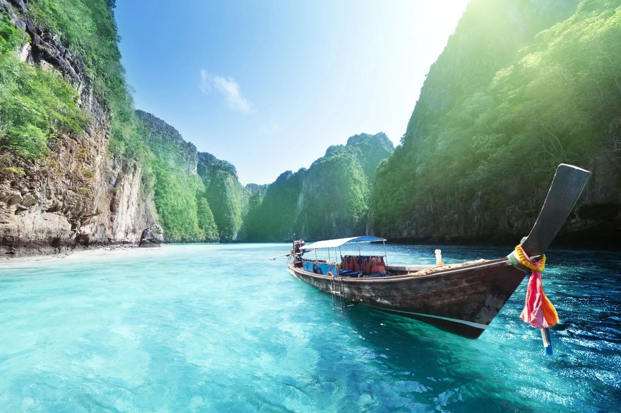 A traditional wooden boat floats on clear turquoise water near lush green cliffs.