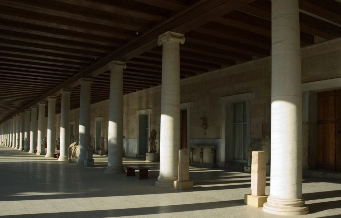 Sunlit corridor with classical columns and benches.