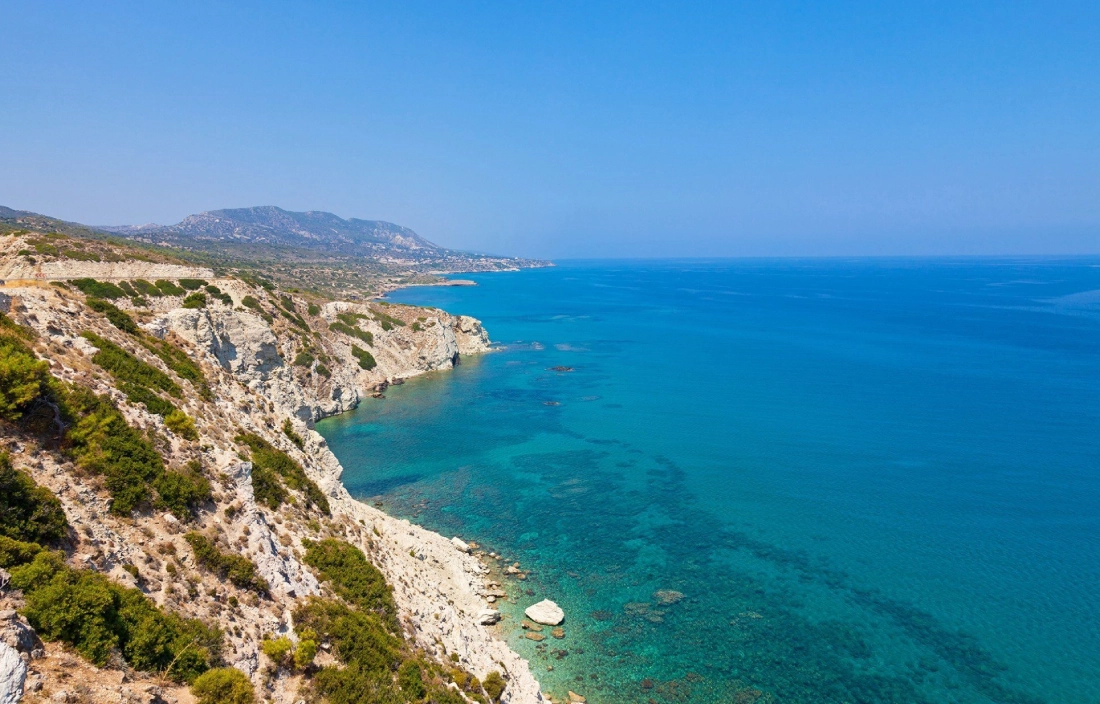 Scenic coastal cliff with clear blue waters under a bright sky.