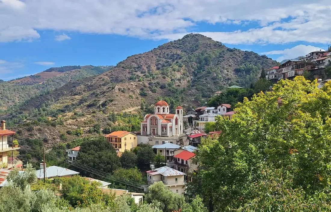 Village nestled in a lush mountainous landscape under a partly cloudy sky.