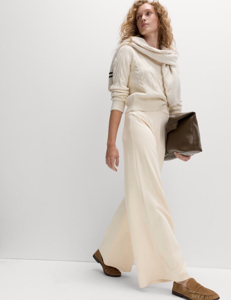 Elegant woman in cream outfit holding a brown clutch.