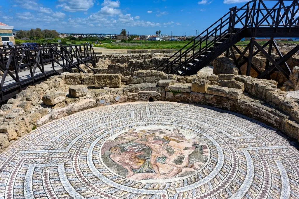 Ancient mosaic with lion design in an archaeological site under blue sky.