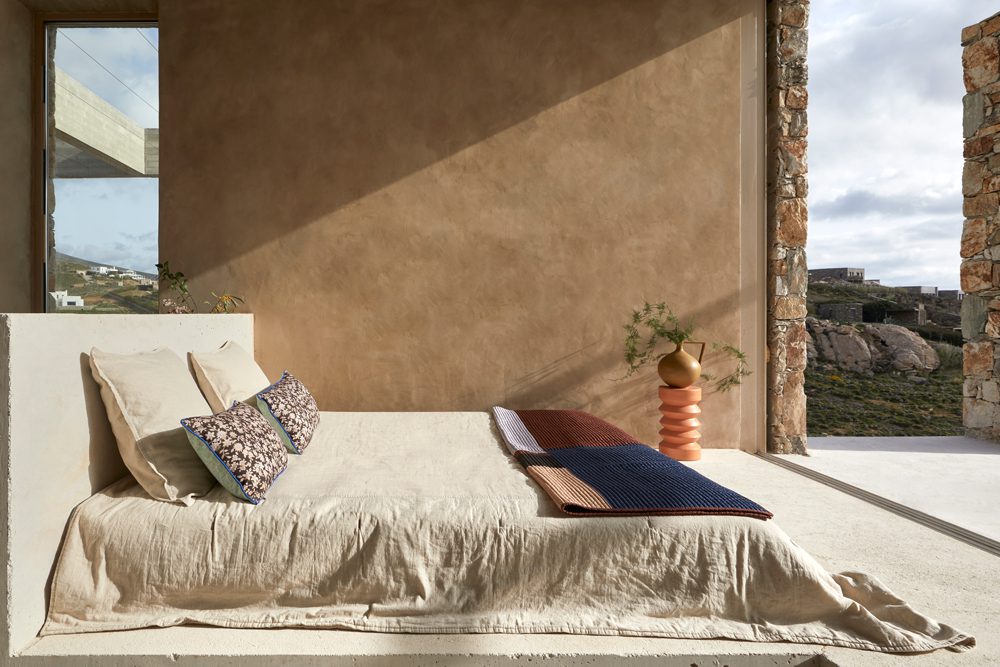 Minimalist bed with cushions against a textured brown wall.