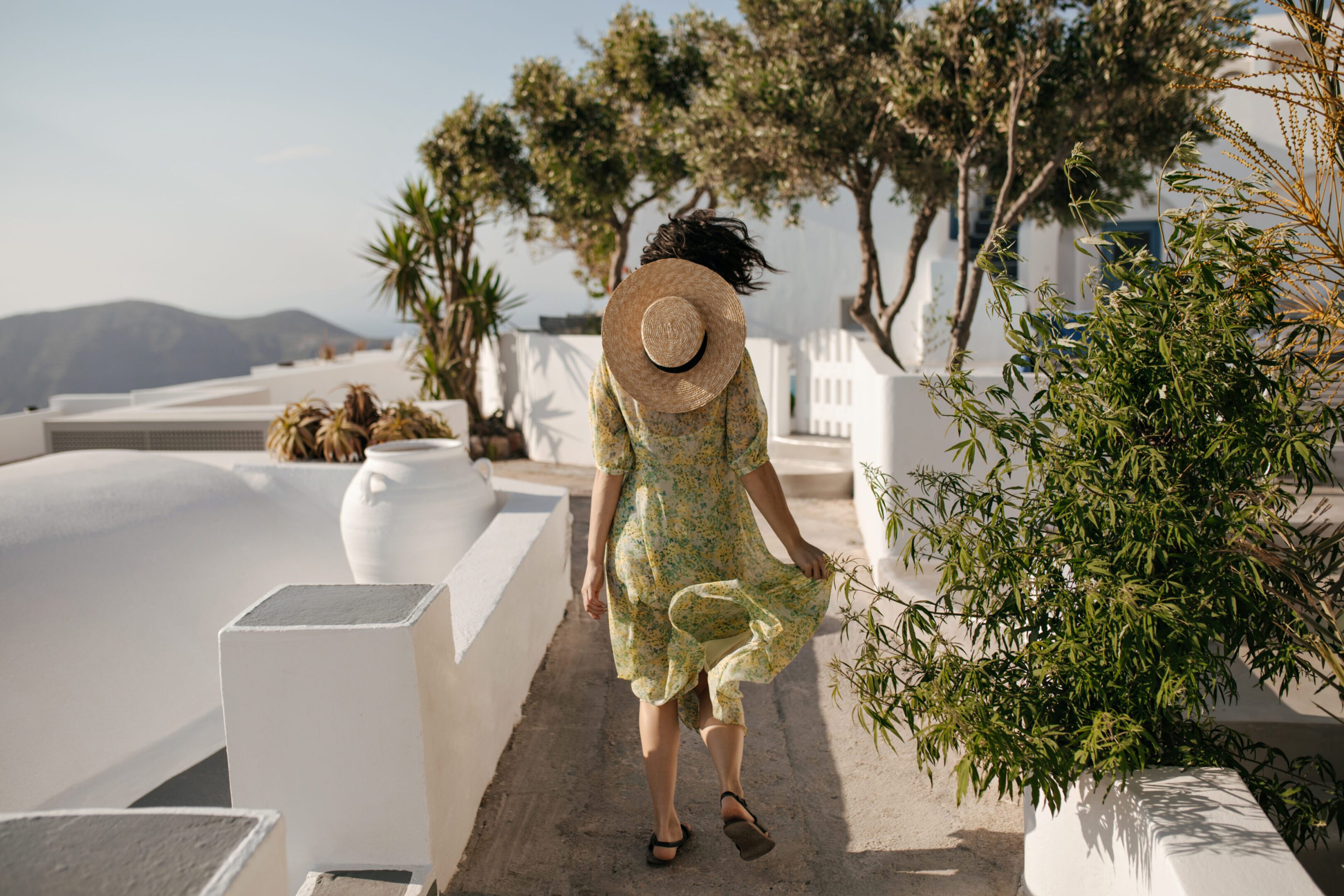 Woman in green dress and hat walking outdoors on a sunny day.