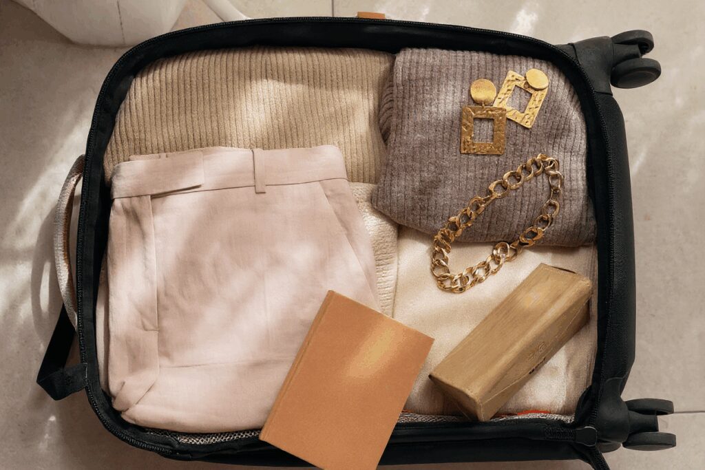 Open suitcase with beige clothing and accessories inside.