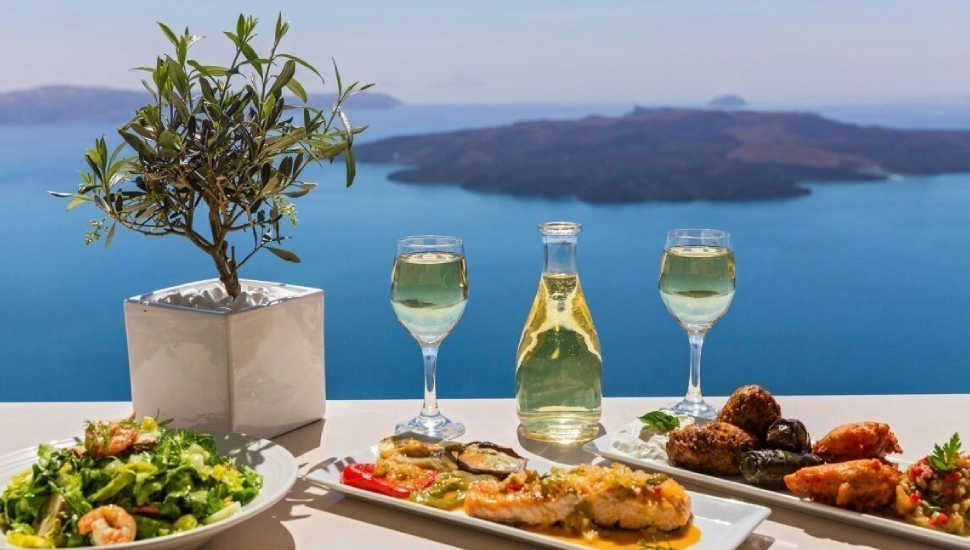 A scenic outdoor meal with wine overlooking a blue sea and islands.