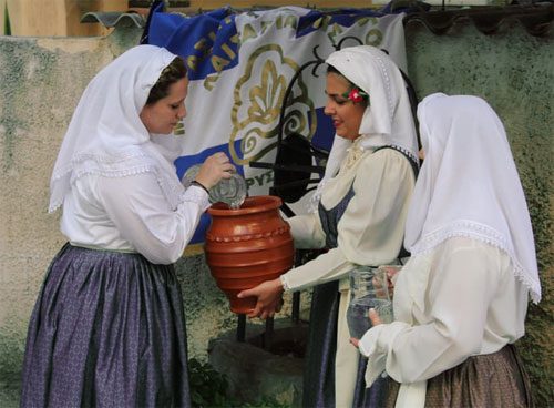 Three women in traditional attire handling a large clay pot.