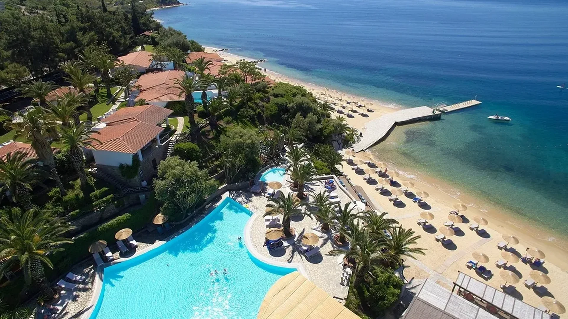 A serene beach resort with a pool and sun loungers by the sea.