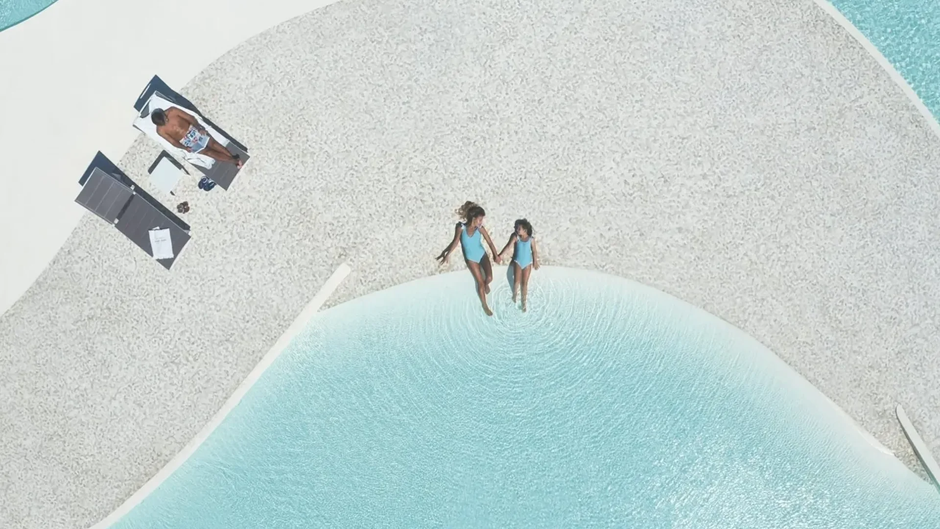 Two women holding hands by a pool on a sandy beach.