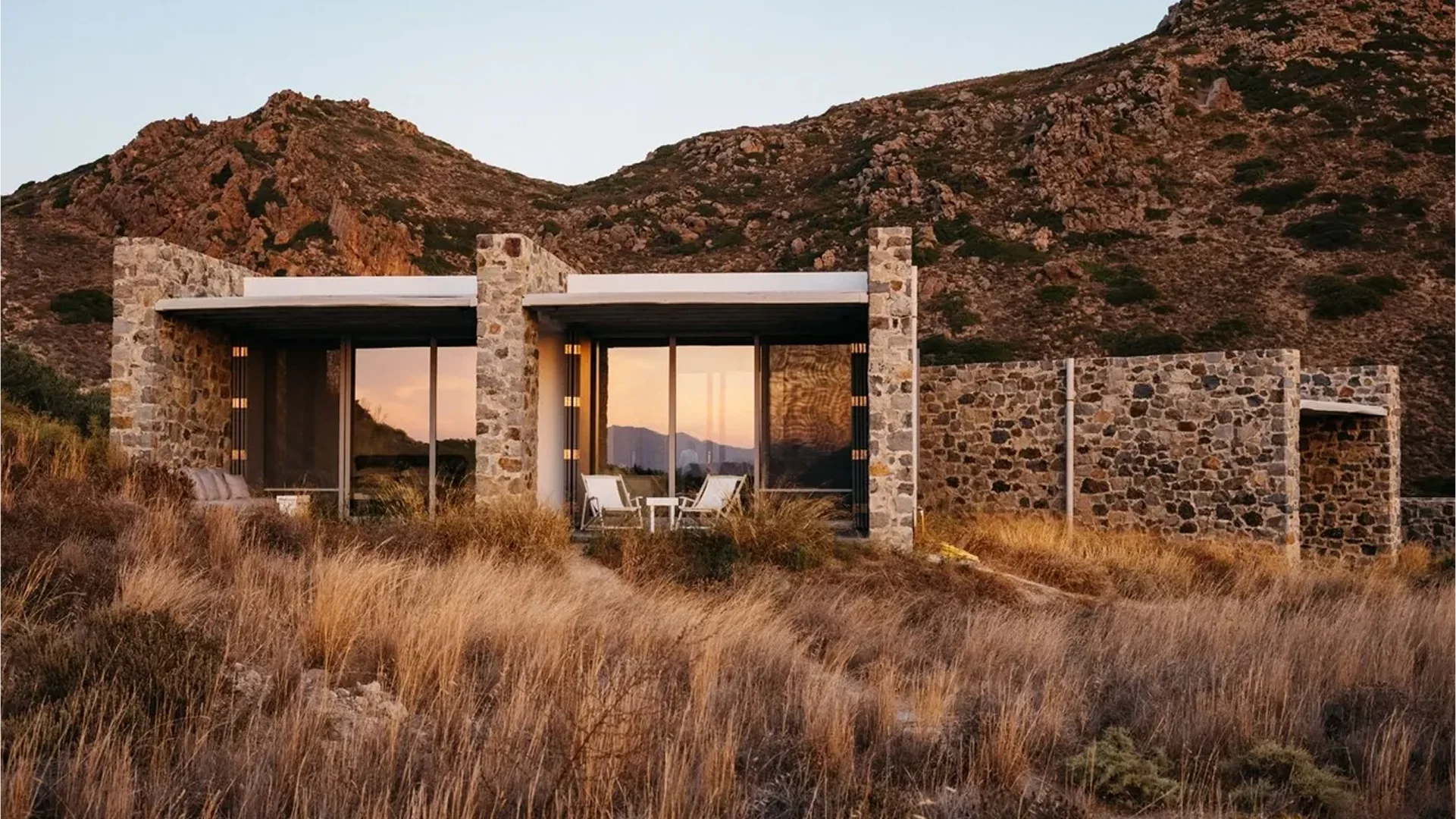 Modern stone house in a dry, grassy landscape at sunset.