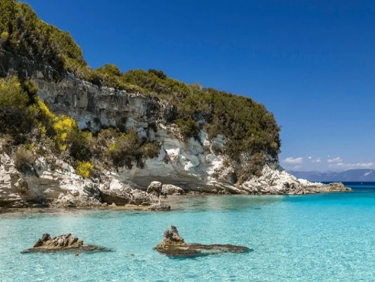Crystal-clear turquoise water meets rocky cliffs under a bright blue sky.