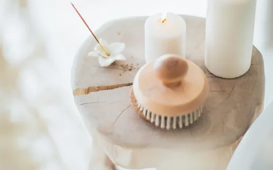 A wooden hairbrush and lit candle on a marble surface with incense.