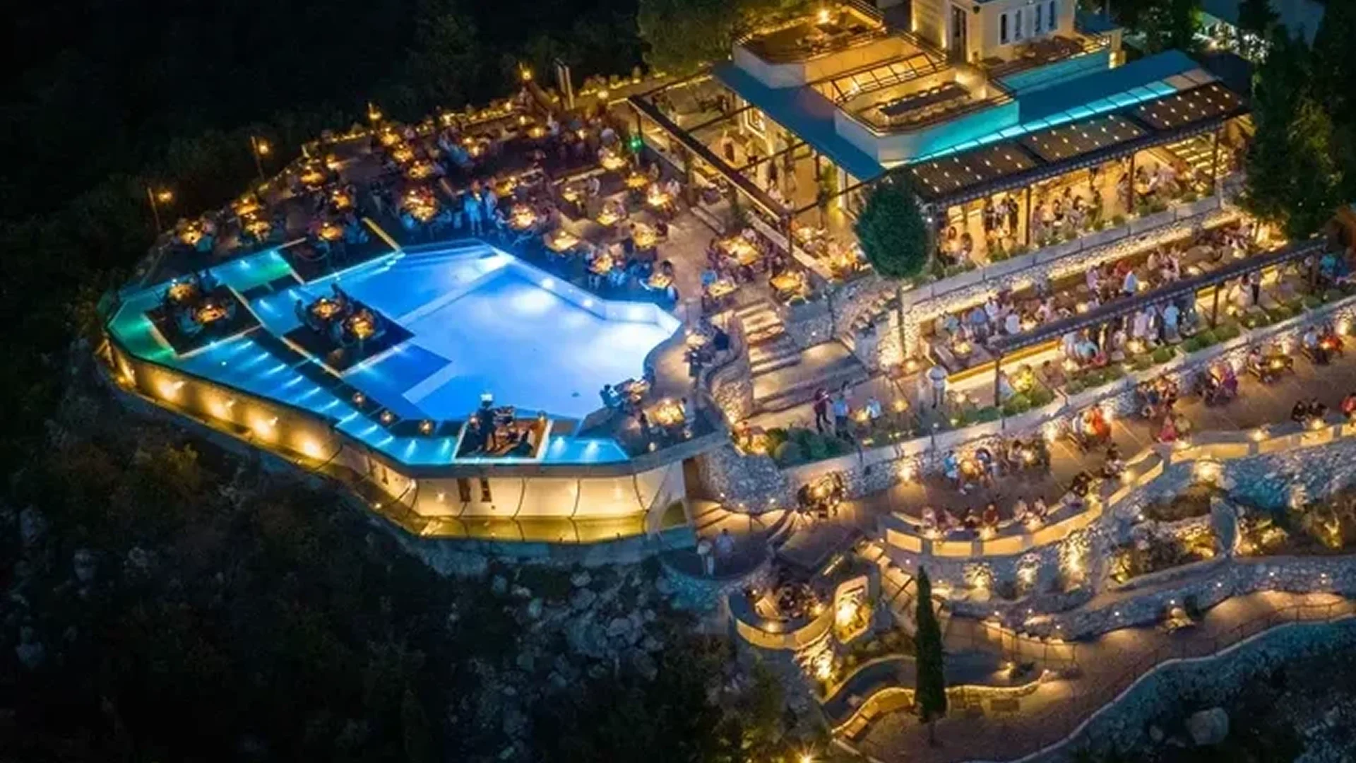 A luxurious, illuminated resort with a large pool at night.