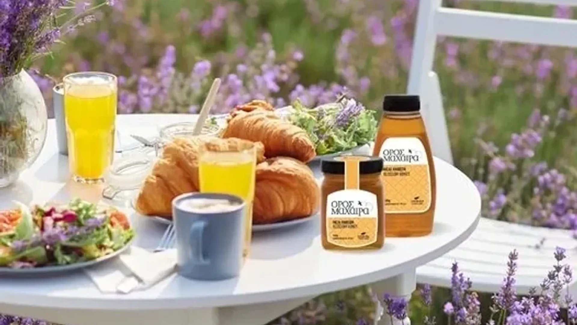 Breakfast table with croissants, coffee, orange juice, and honey jars outdoors.