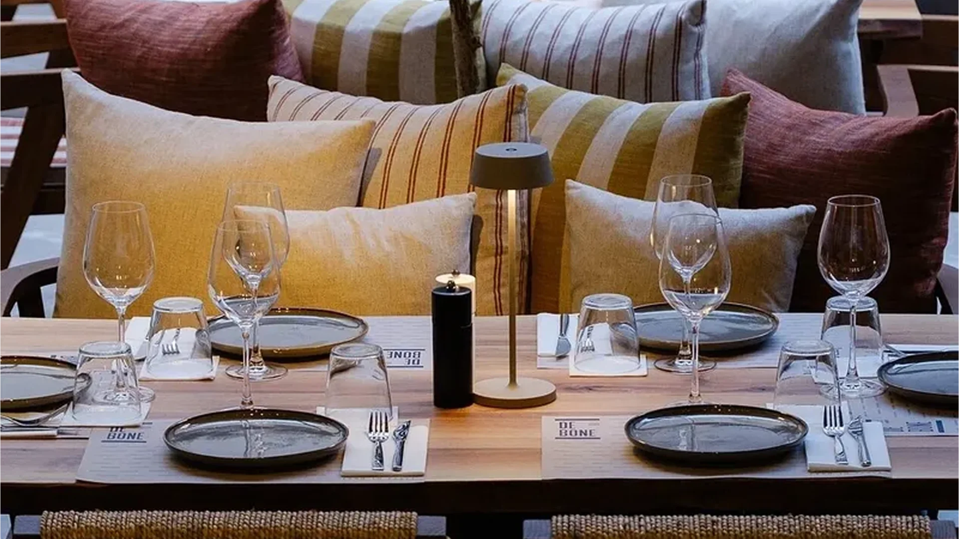 Elegant dining table set with glassware and cushions.