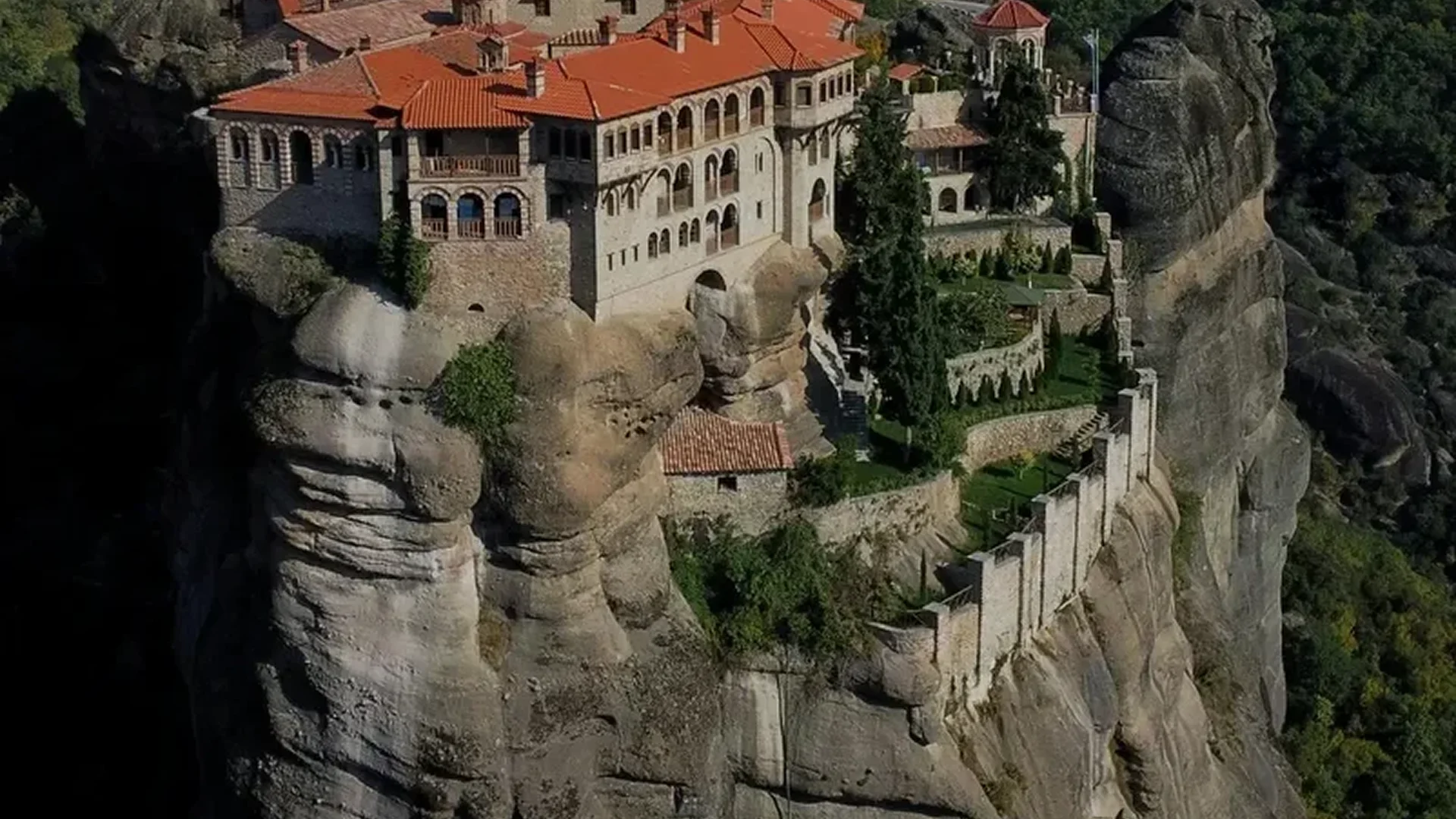 Ancient monastery perched atop rocky cliffs with red-tiled roofs.