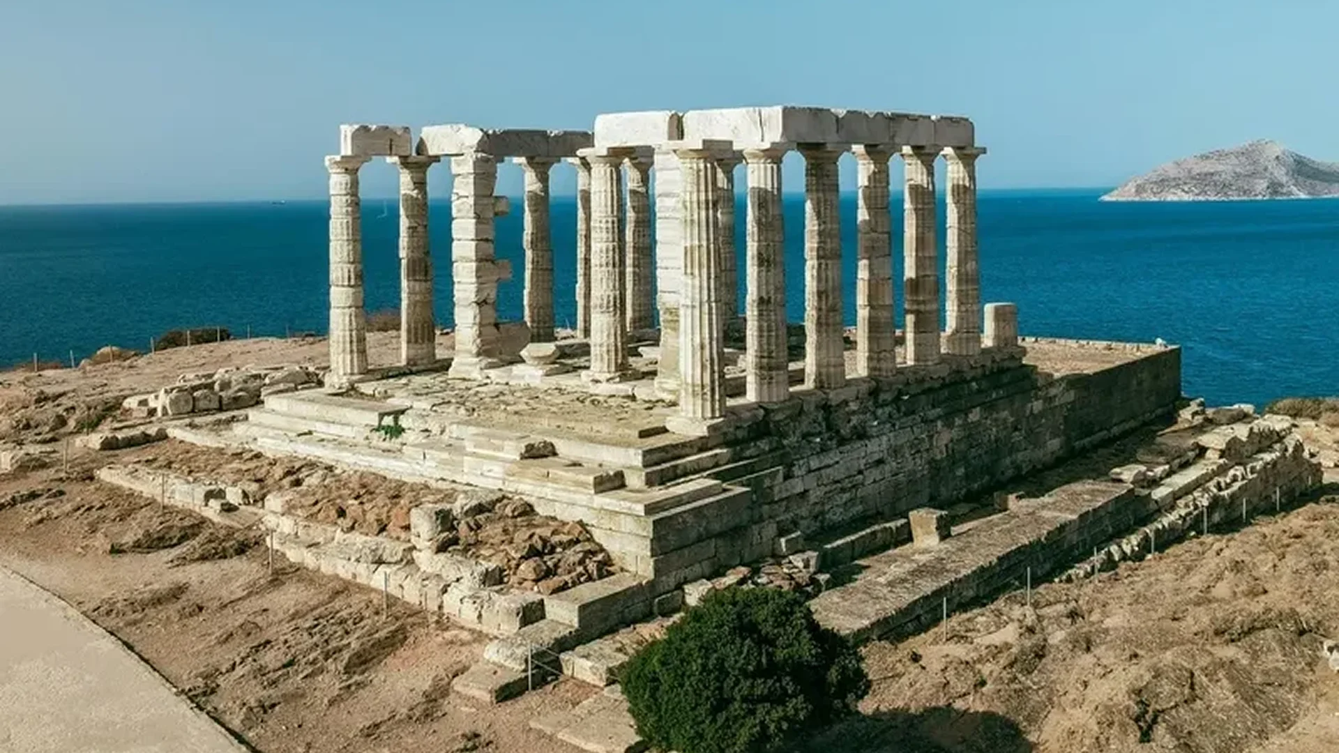Ancient Greek temple ruins by the sea under a clear sky.