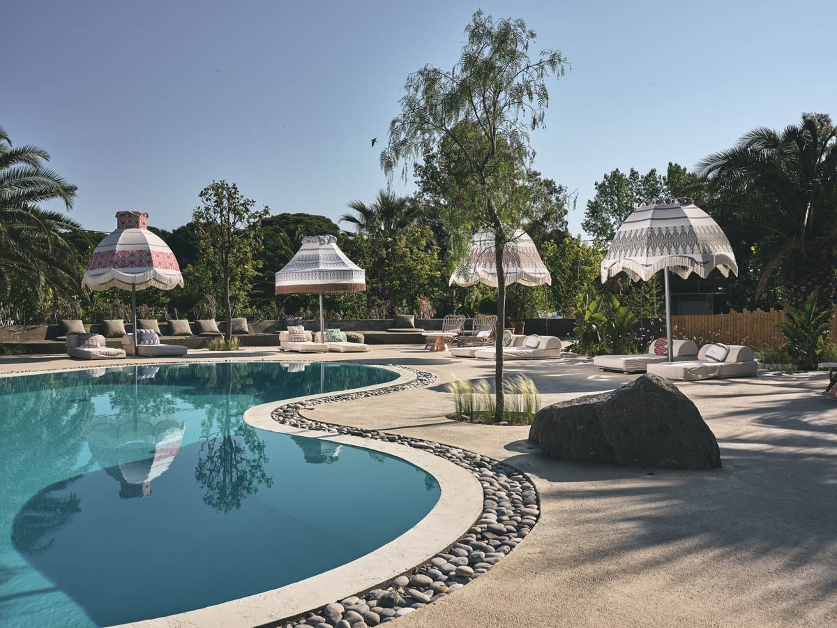 A serene outdoor pool area with unique white fringed umbrellas and lounge chairs under a clear sky.