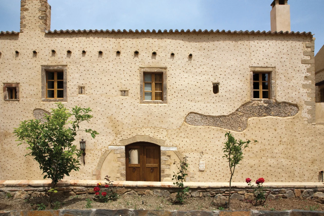 Rustic stone house with wooden windows and small trees outside.