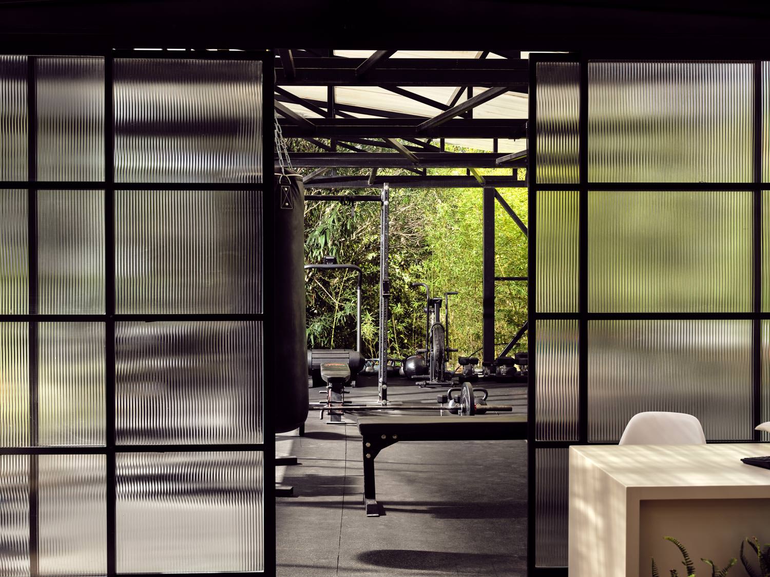 View through glass panels into a serene gym space with natural light and greenery.