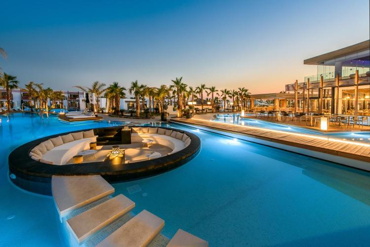 Luxury outdoor pool area with modern seating and palm trees at sunset.