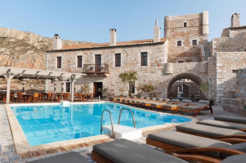 Historic stone building with a clear blue pool and lounge chairs under a sunny sky.