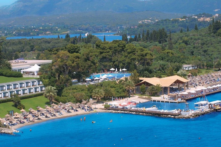 A large resort pool with lounge chairs and umbrellas surrounded by greenery and mountains.