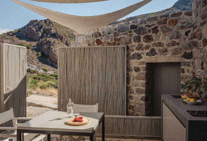 Outdoor dining setup with stone wall and canopy in a desert landscape.
