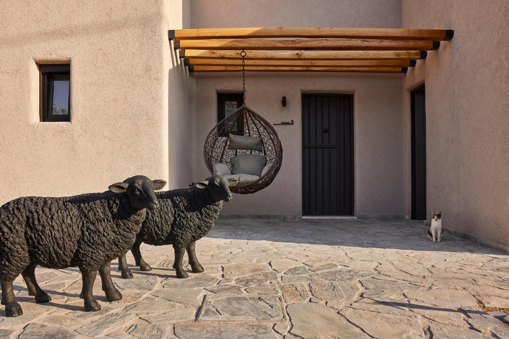 Two black sheep statues stand on a stone patio near a hanging chair and a closed door.