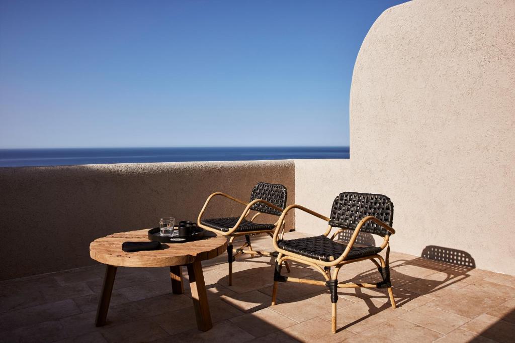 Two chairs and a table on a sunny terrace with ocean view.