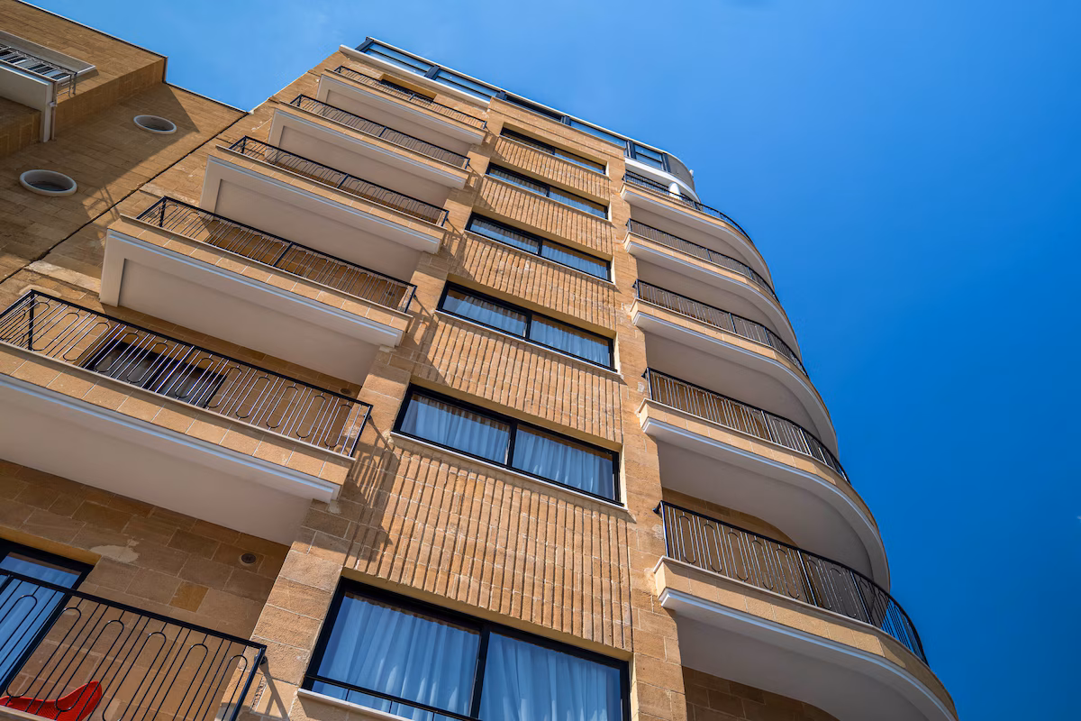 Upward view of a modern beige apartment building against a clear blue sky.