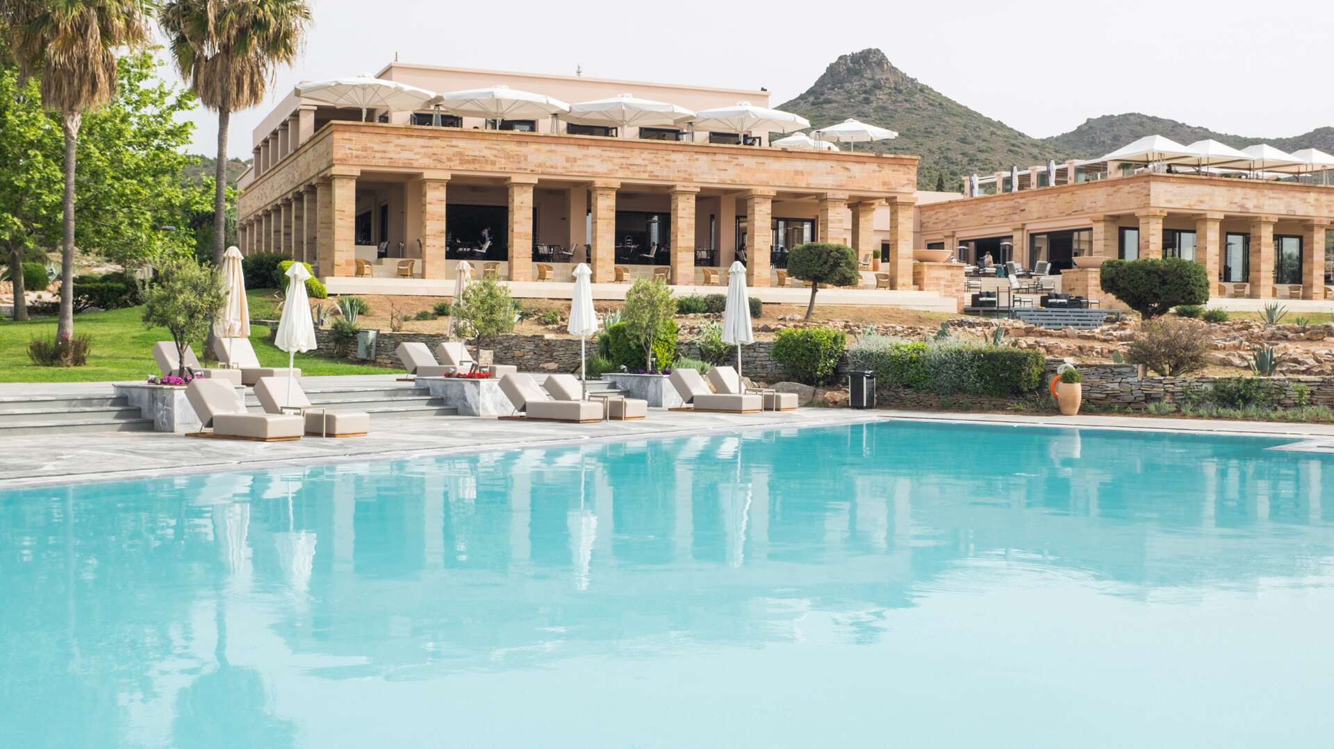 Luxurious villa with a large swimming pool and lounge chairs under umbrellas.