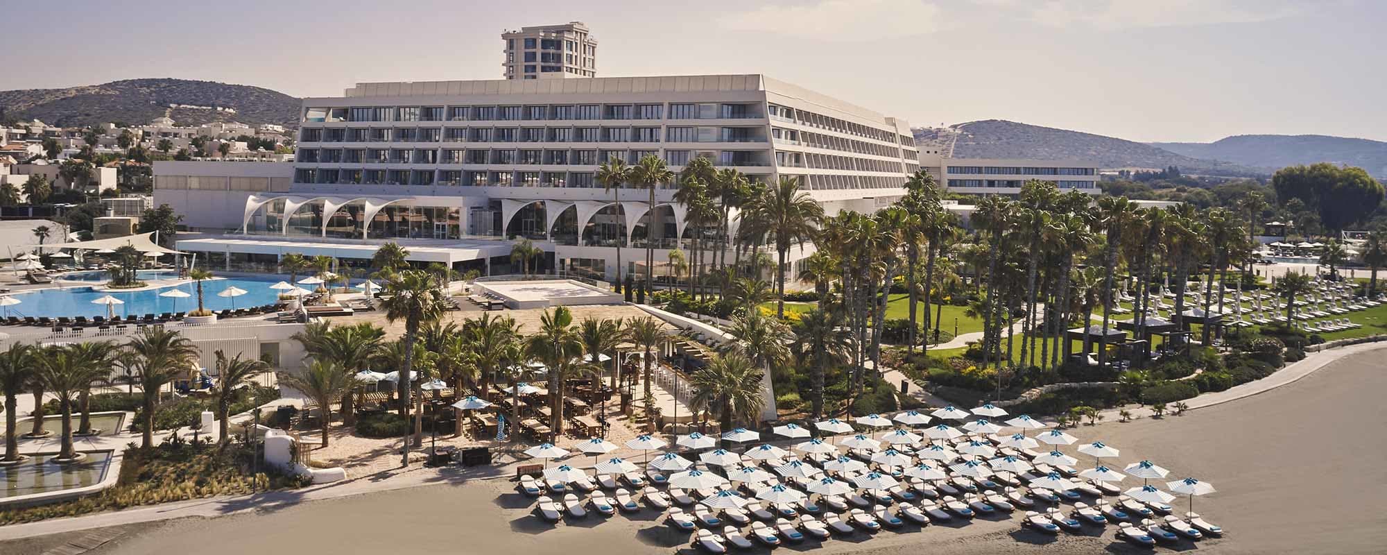 Luxurious beachfront hotel with pools and palm trees under a clear sky.