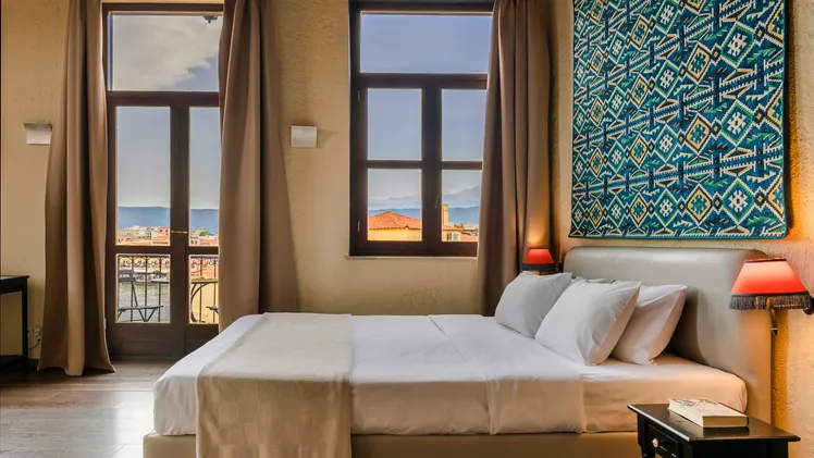 Cozy bedroom with a scenic window view of rooftops and sea.