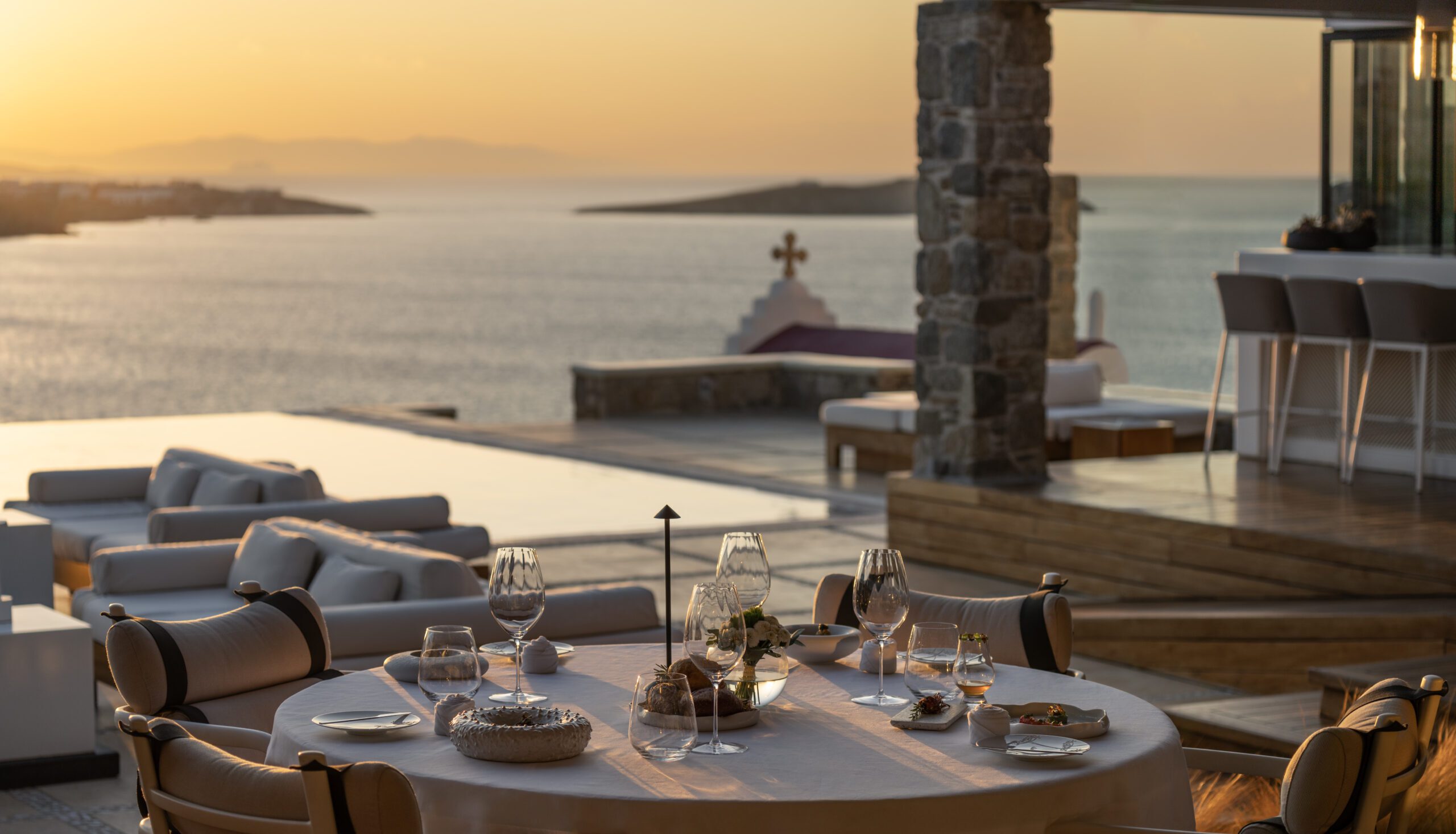 Elegant seaside dining setup at sunset with a view of a small chapel.