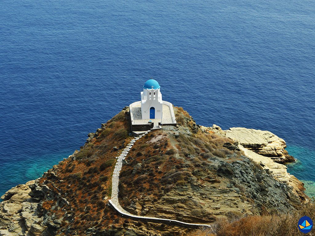 A small white chapel with a blue dome on a rocky cliff by the sea.