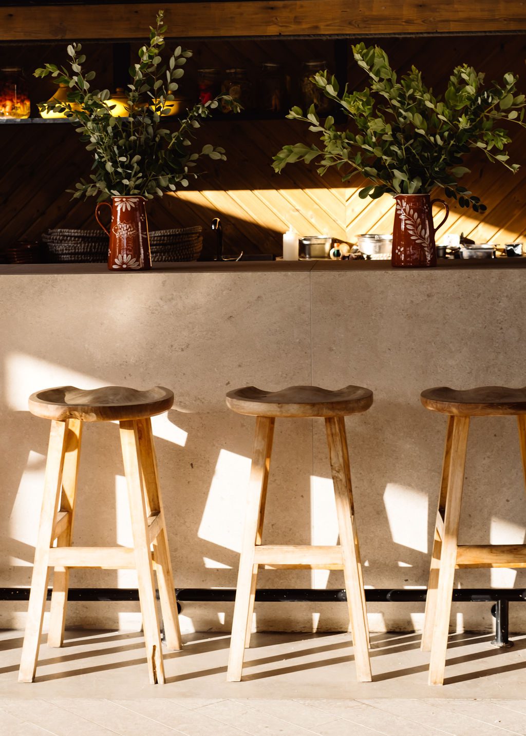 Four wooden stools lined up against a white wall under warm sunlight.