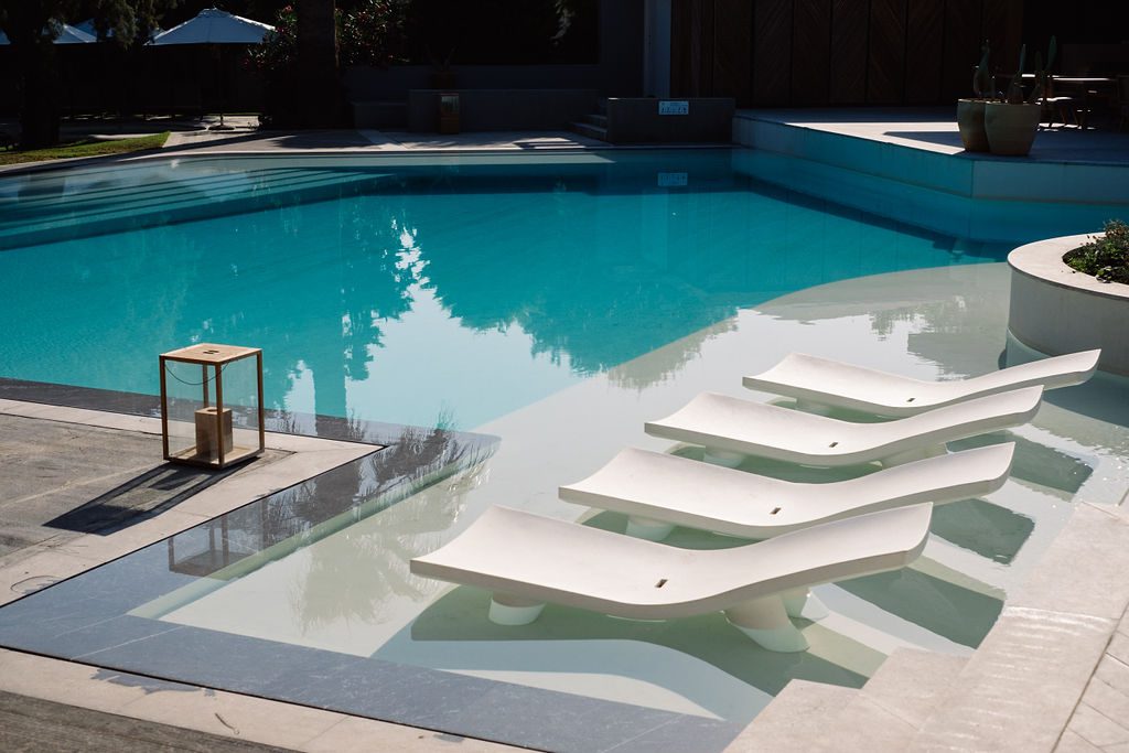 Modern poolside with white loungers partially submerged in water.