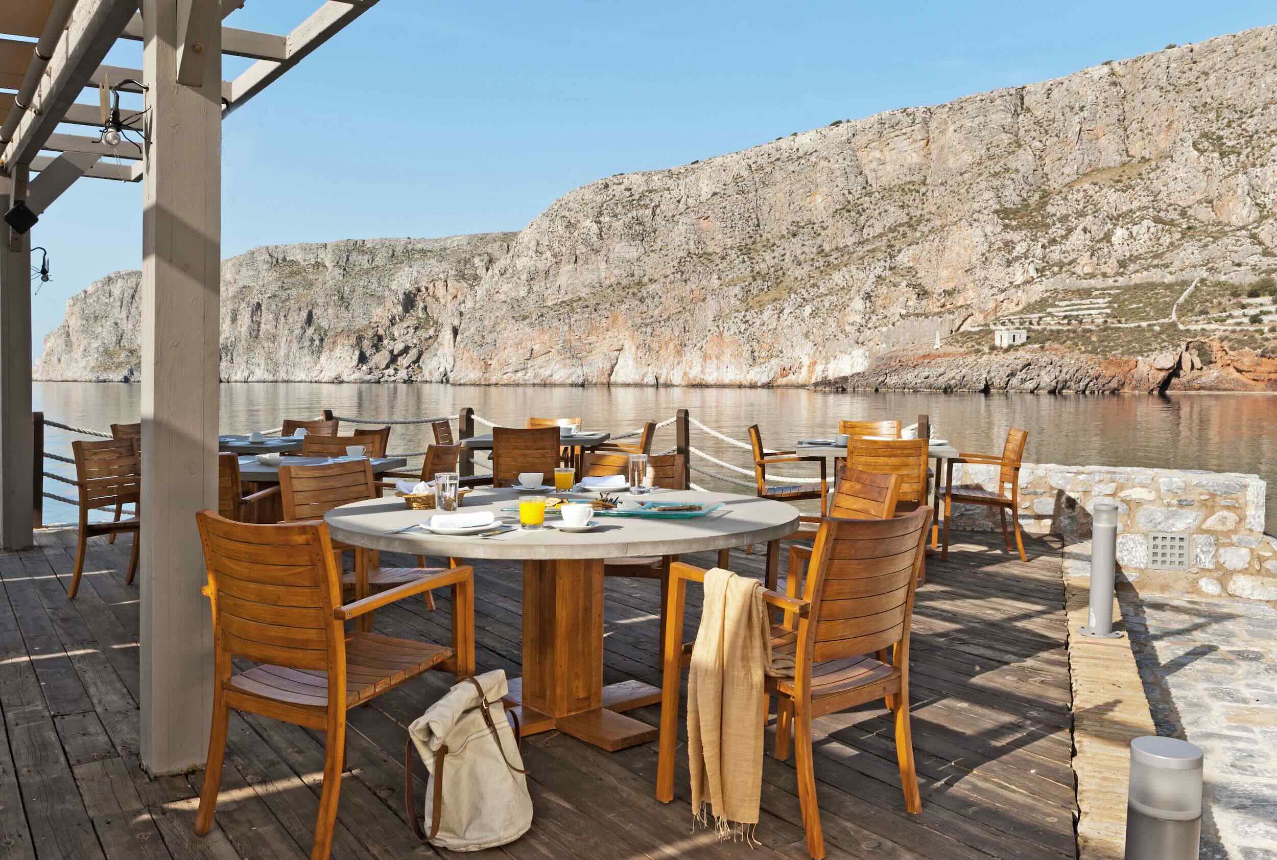 Outdoor dining area with wooden chairs and tables overlooking rocky cliffs.