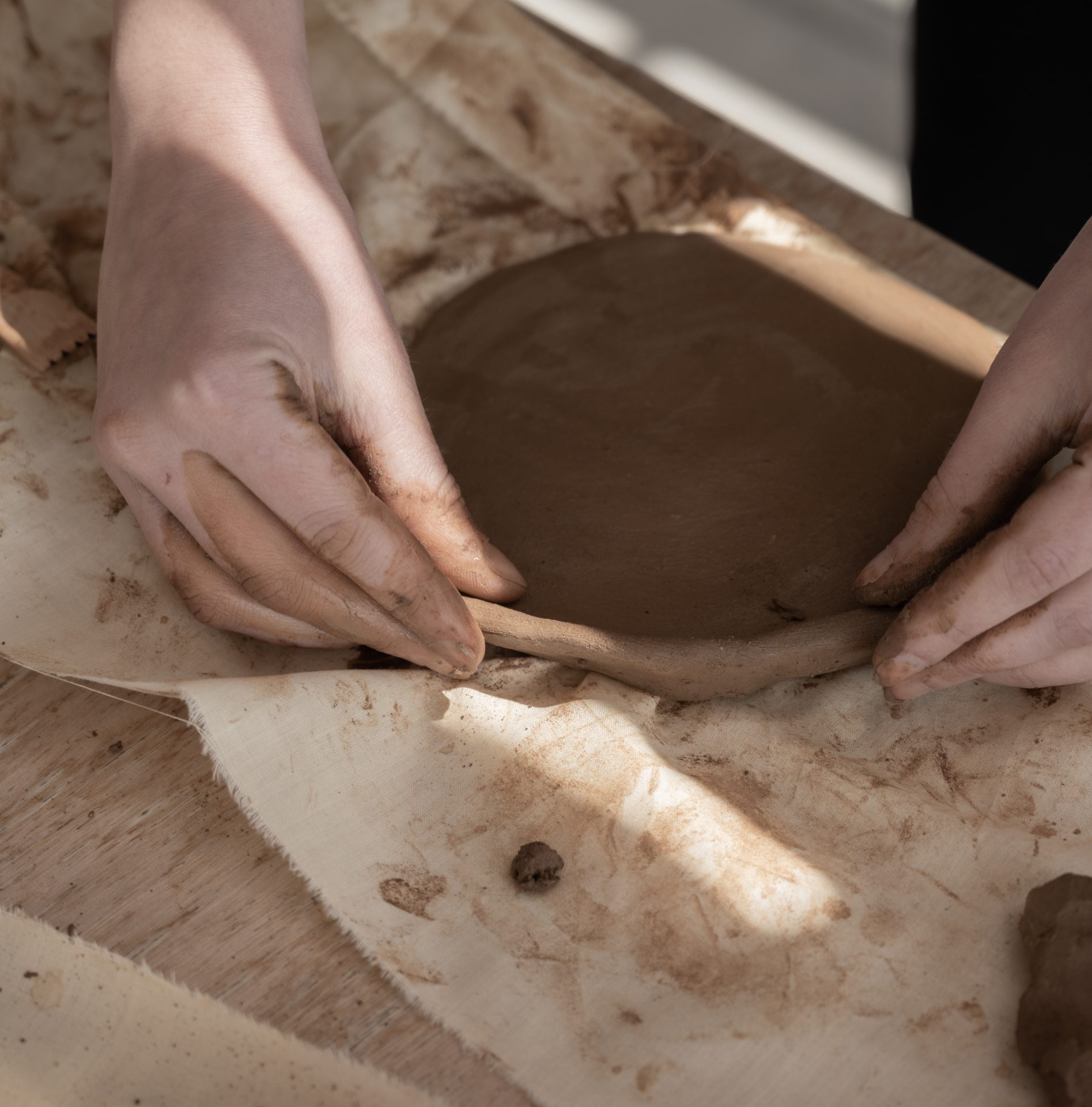 Hands shaping wet clay on a wooden surface.