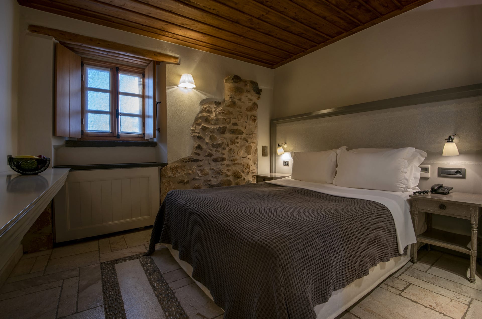 Cozy bedroom with rustic stone wall and wooden ceiling.