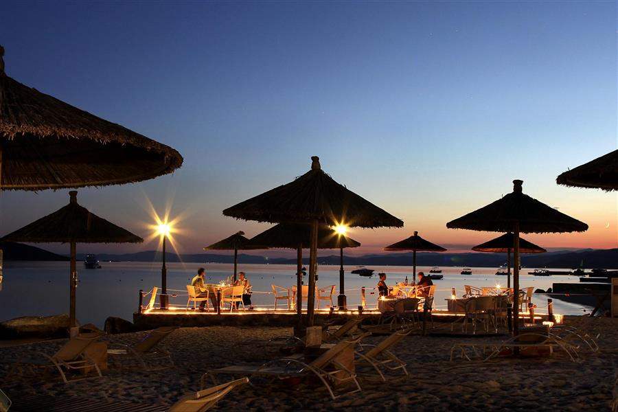 People dining under umbrellas at a beach during sunset.
