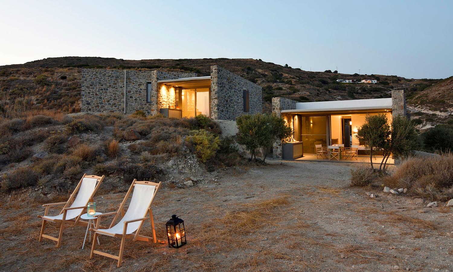 A cozy stone house with warm lights in a desert landscape at dusk.
