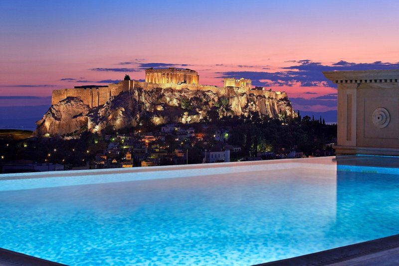 Illuminated Acropolis at sunset beside a glowing pool.