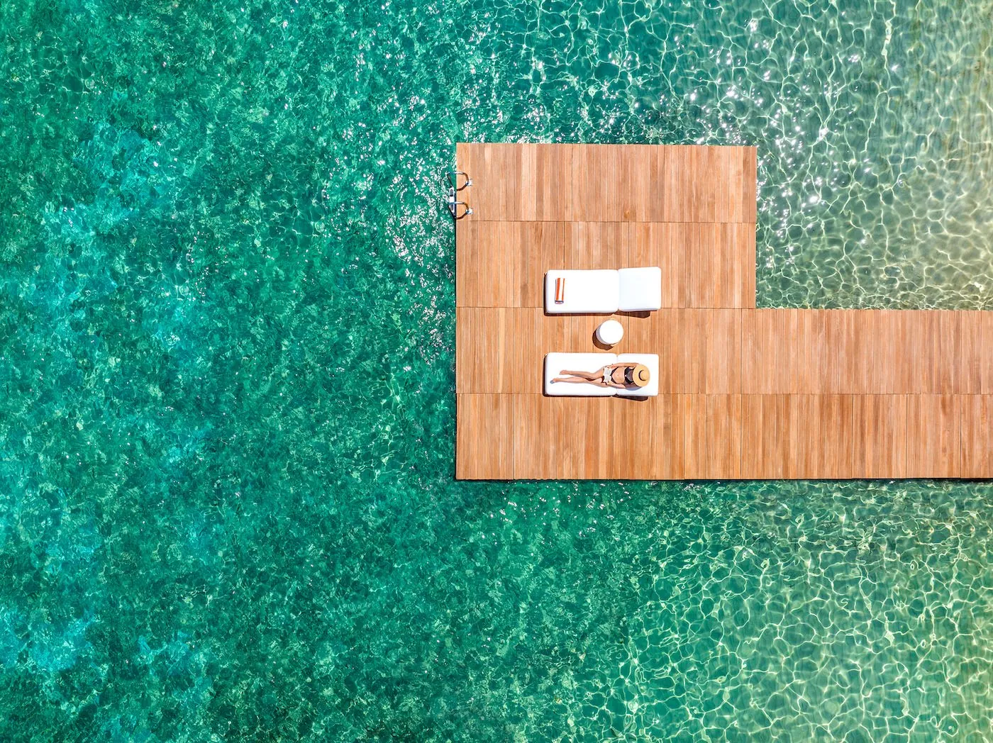 A wooden dock with lounge chairs over clear turquoise water.