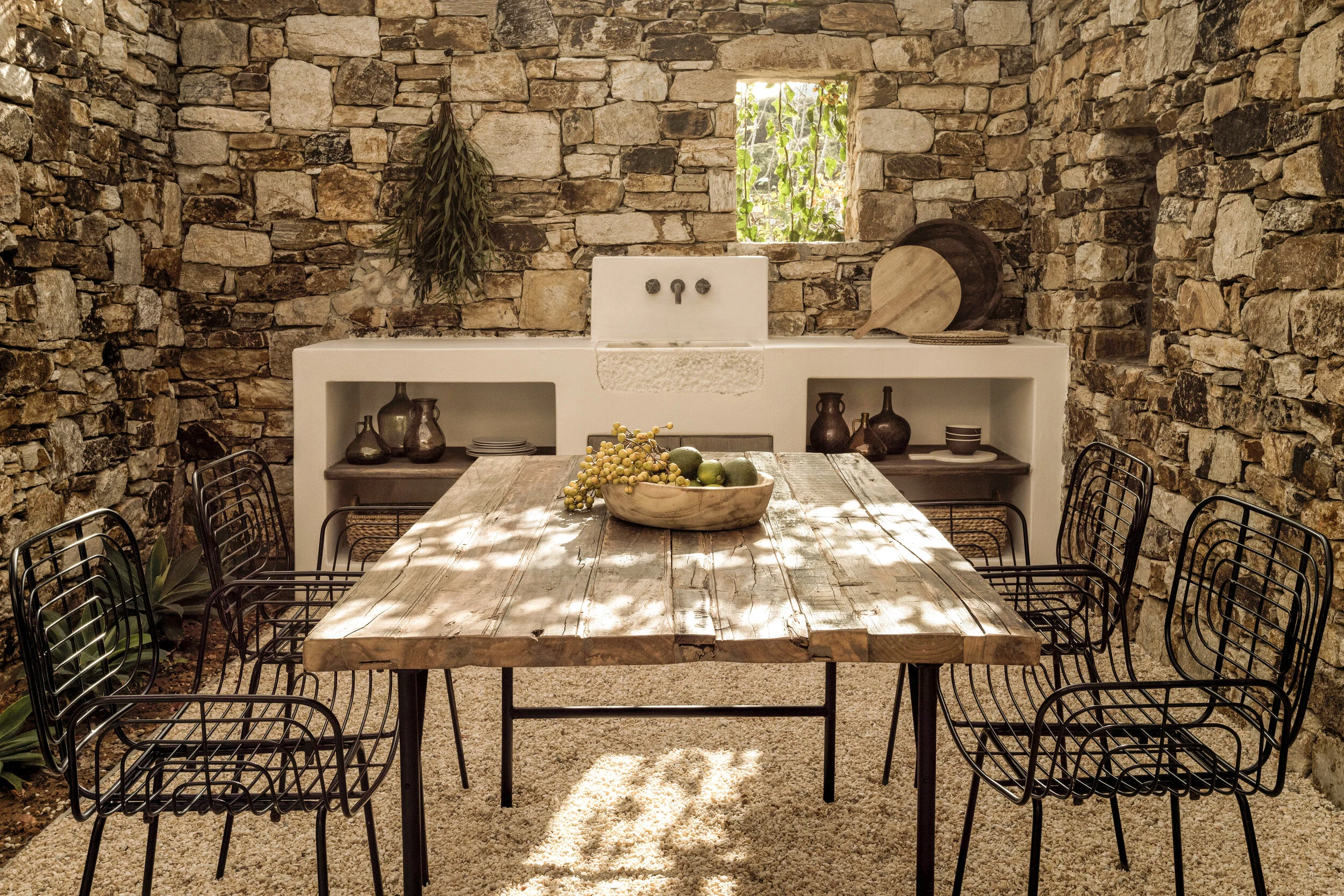 Cozy rustic dining area with wooden table and chairs under dappled sunlight.