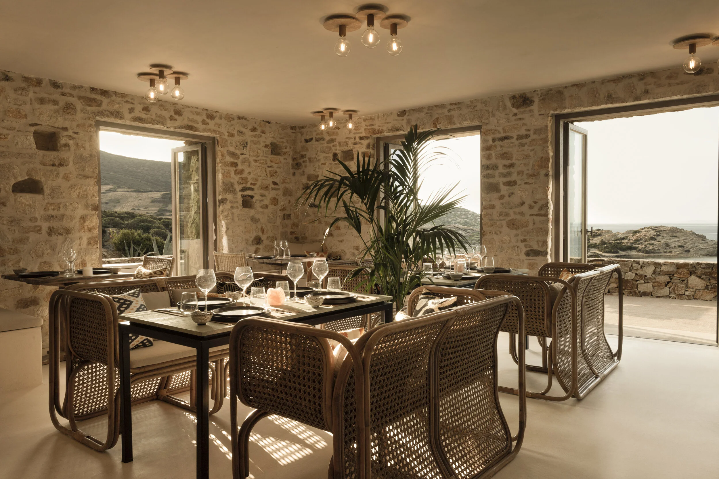 Cozy sunlit dining area with rustic stone walls and wicker chairs.