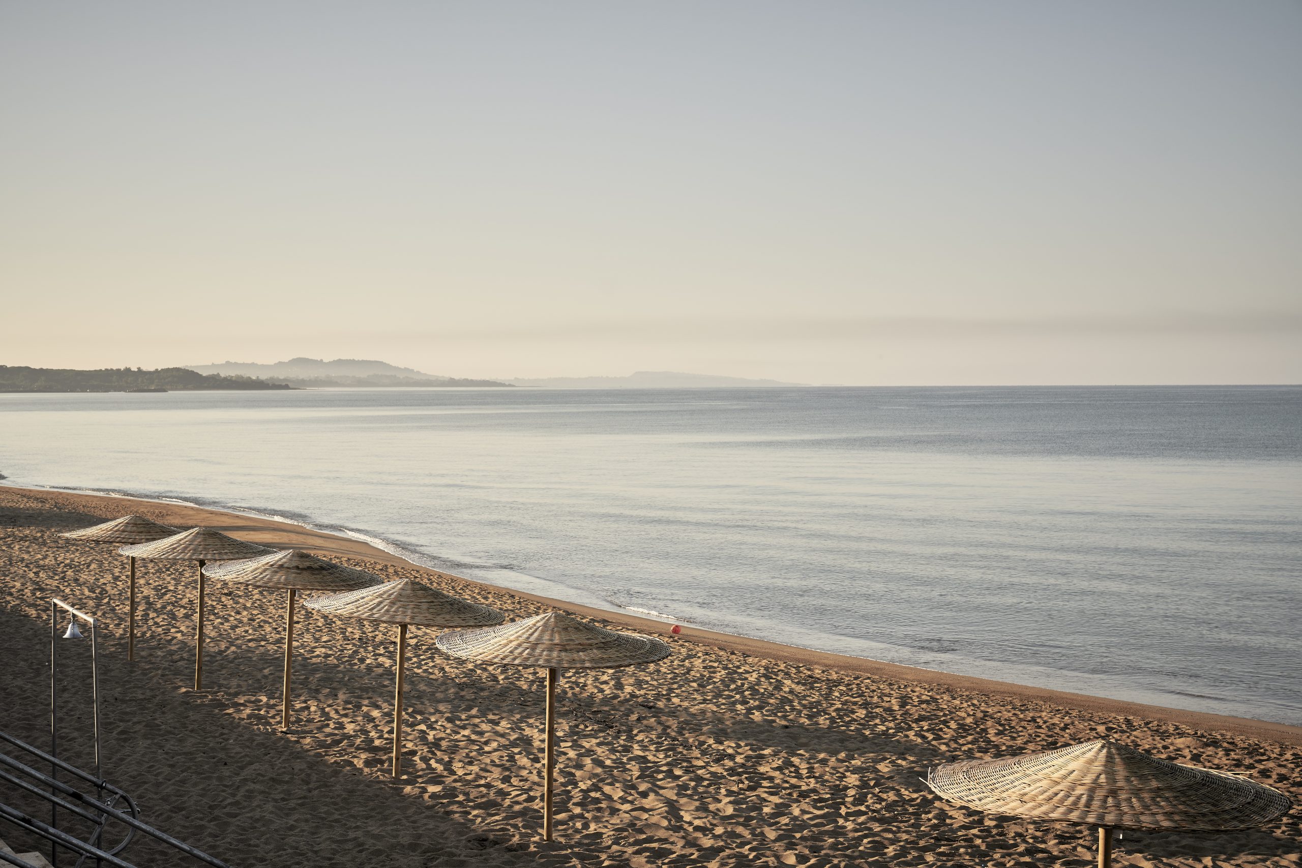 Empty beach chairs lined up along a calm shoreline at sunset.
