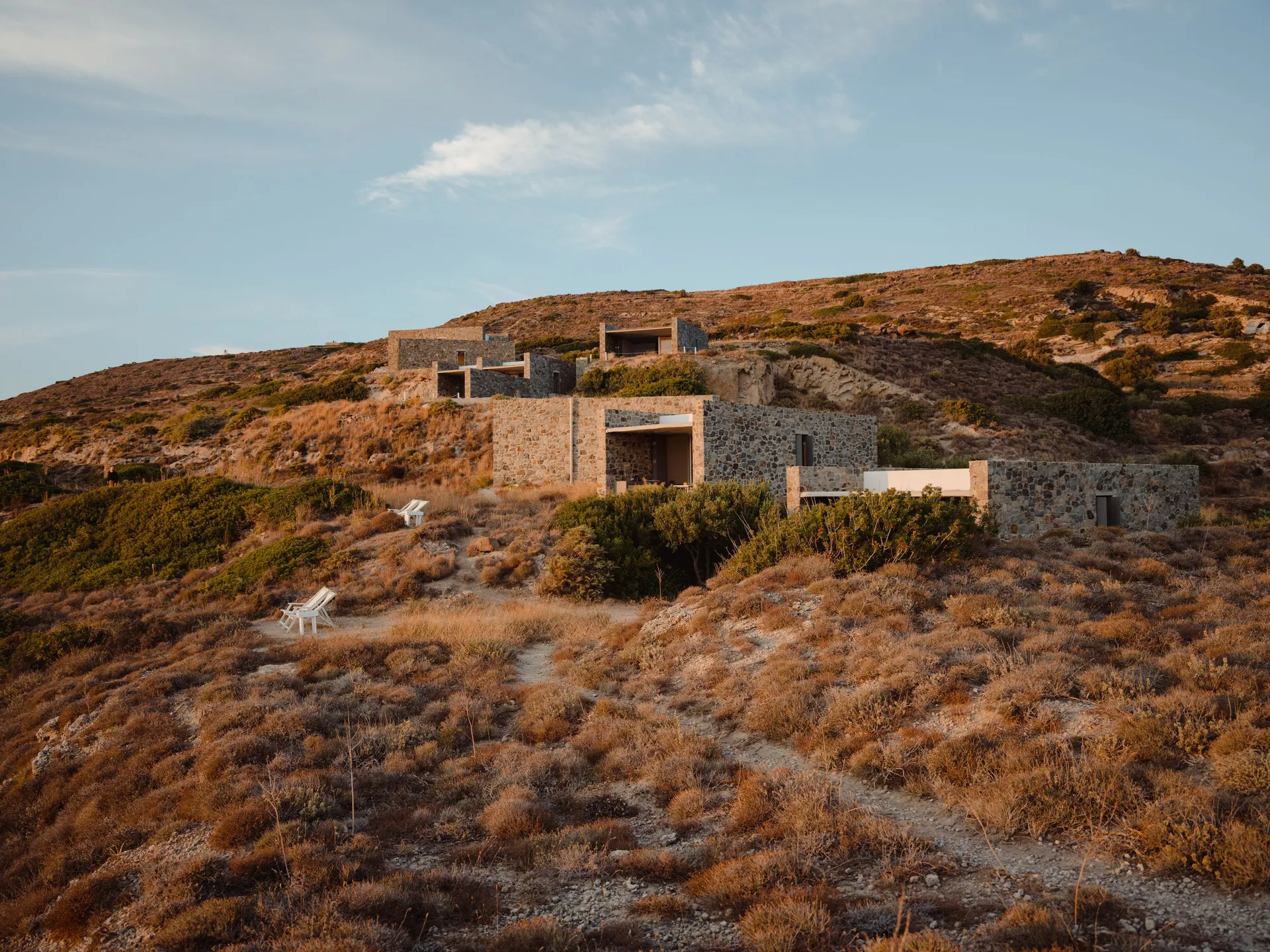 A rustic concrete house on a dry, rocky hillside under a cloudy sky.